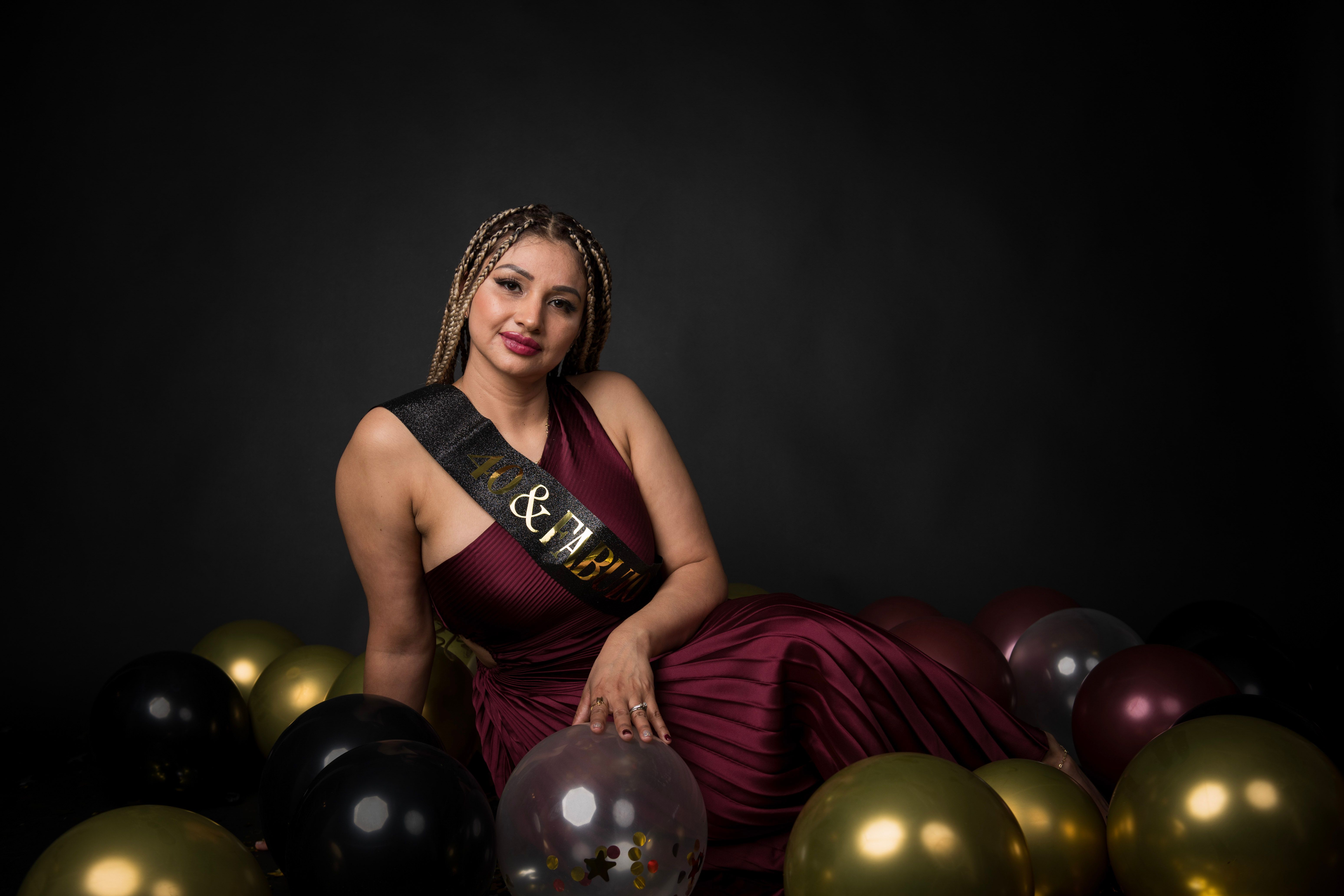 Woman posing for a fortieth-birthday portrait among black and gold balloons.