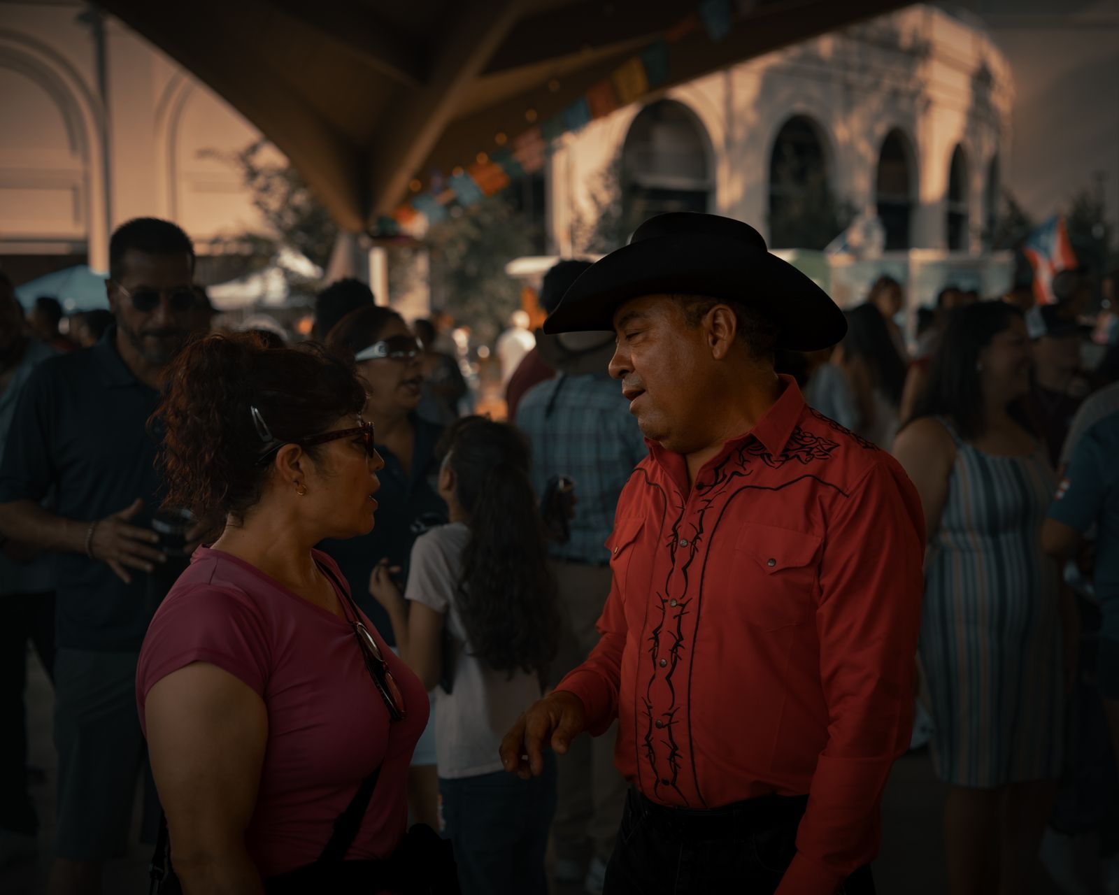 Neighbors talking at a cultural street festival surrounded by other attendees.