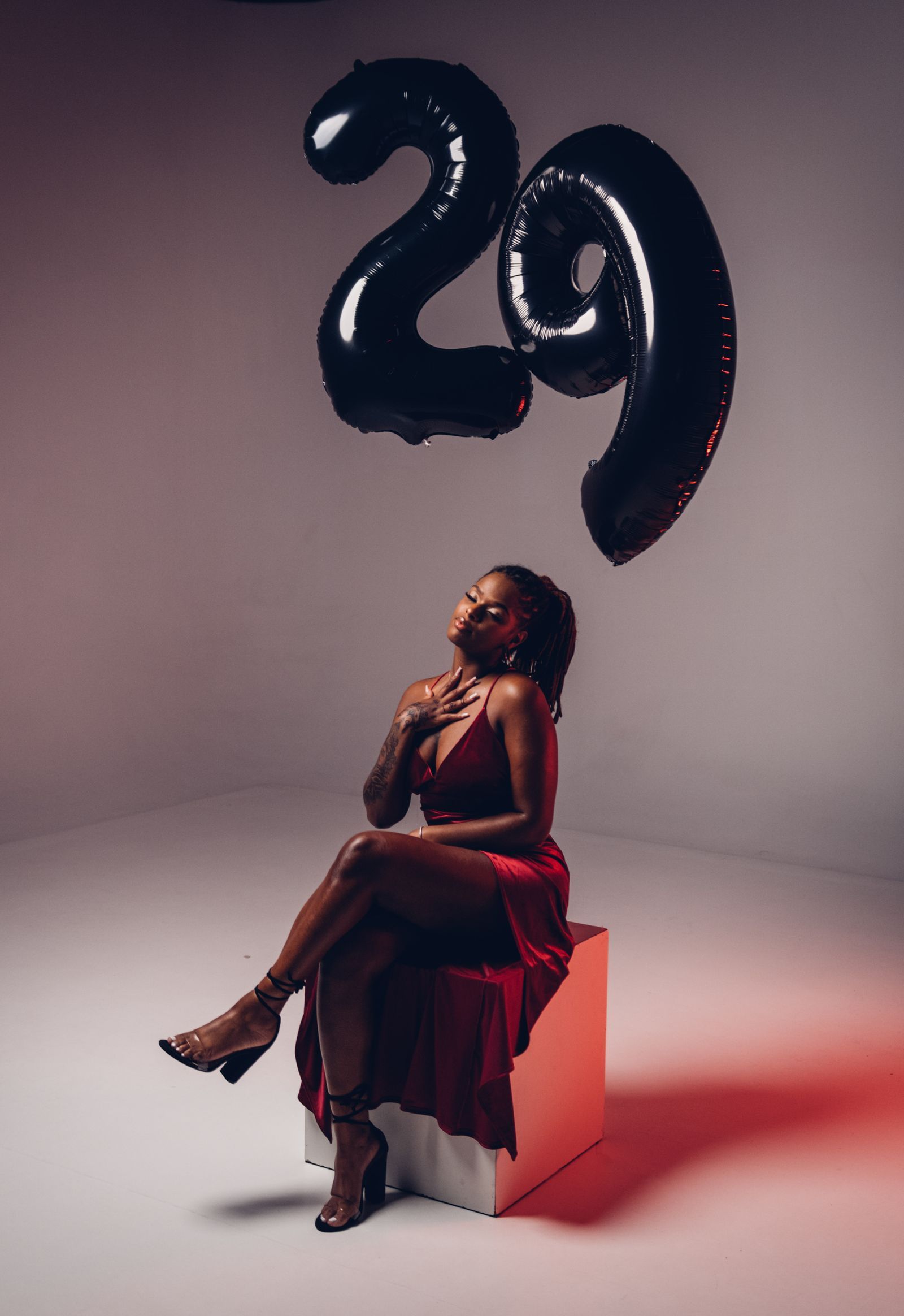 Woman in a red dress posing beneath twenty-ninth-birthday balloons.