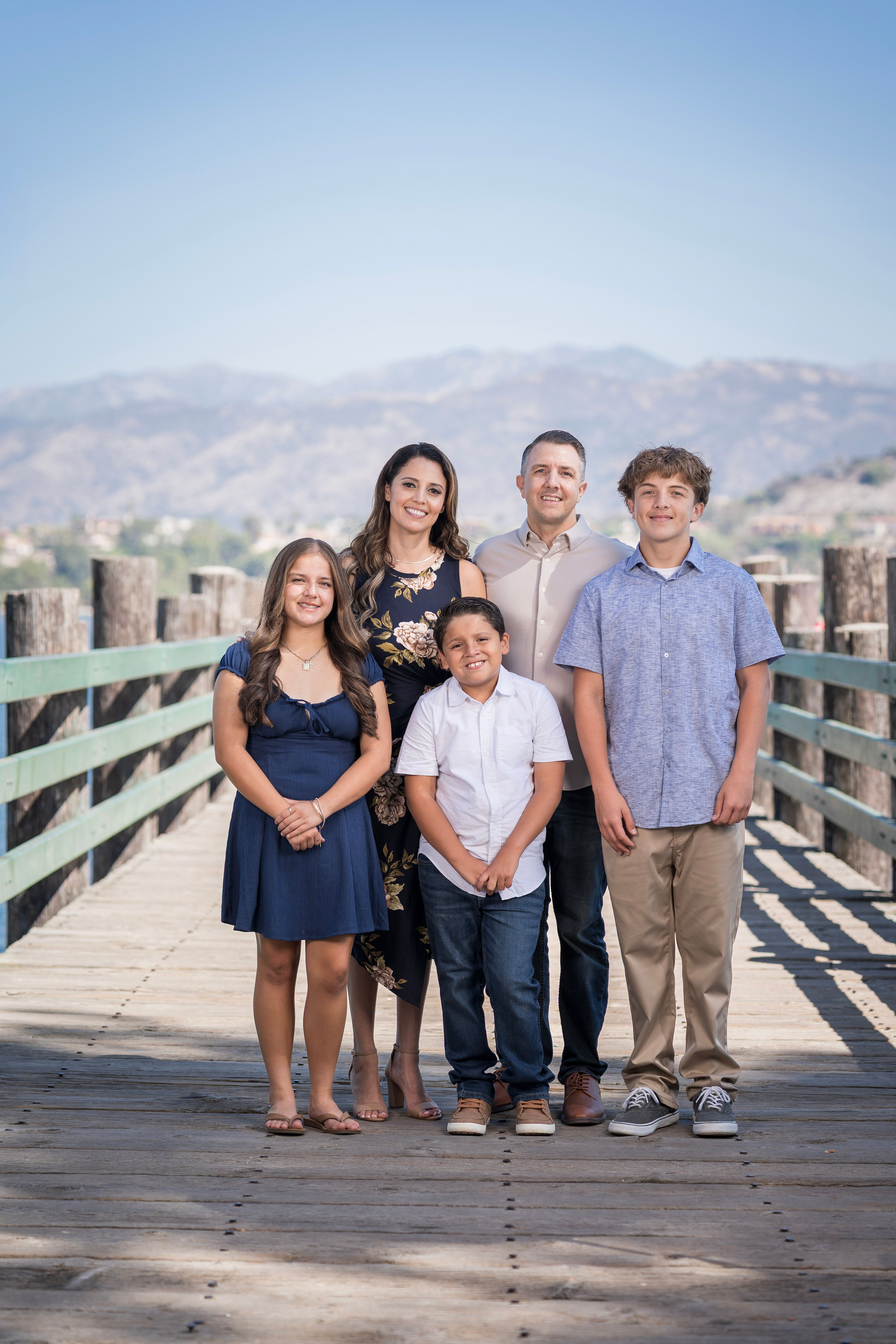Family of five posing together beside a lake on a sunny day.