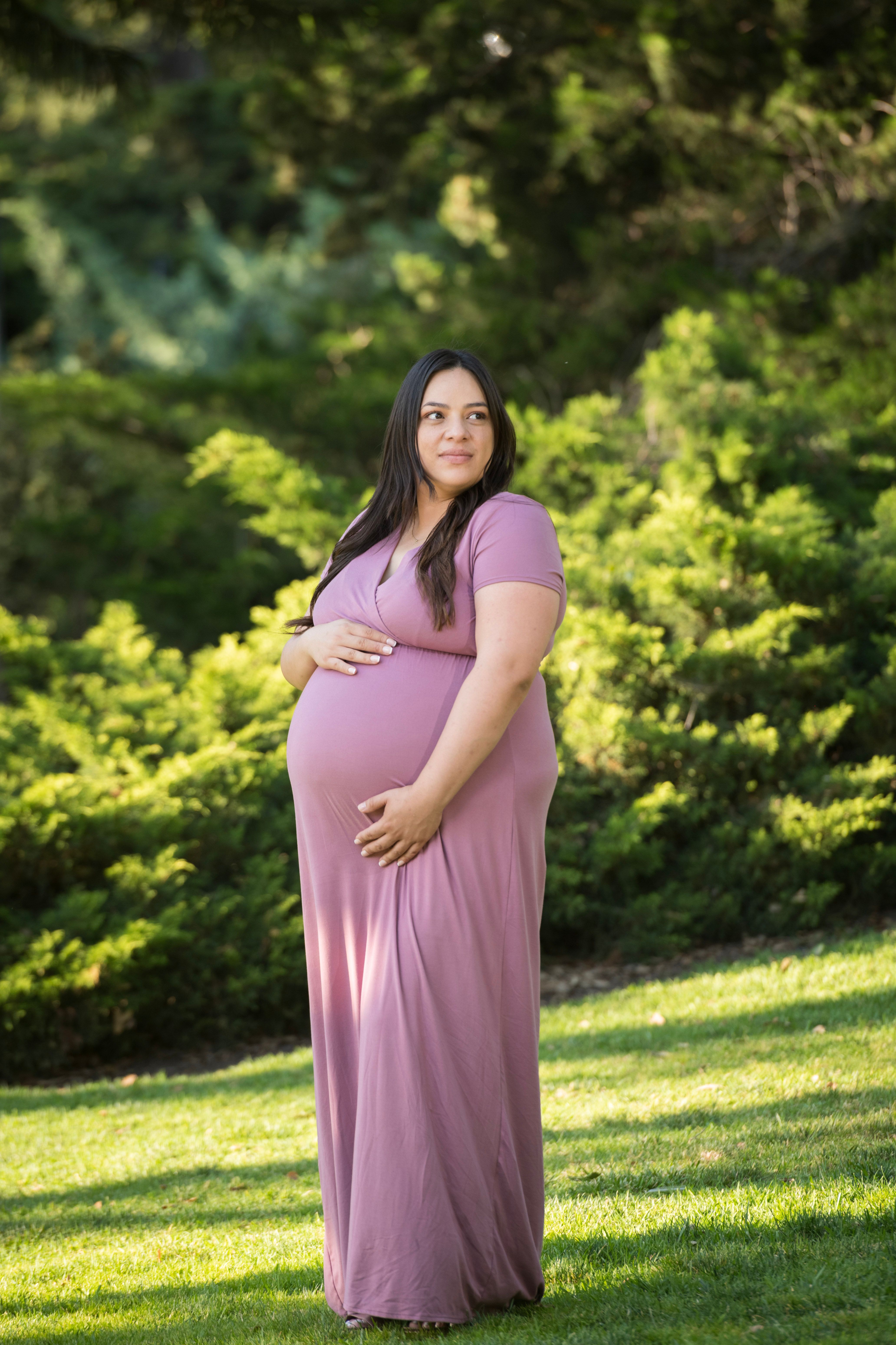 Expectant mother posing in a softly lit garden portrait.
