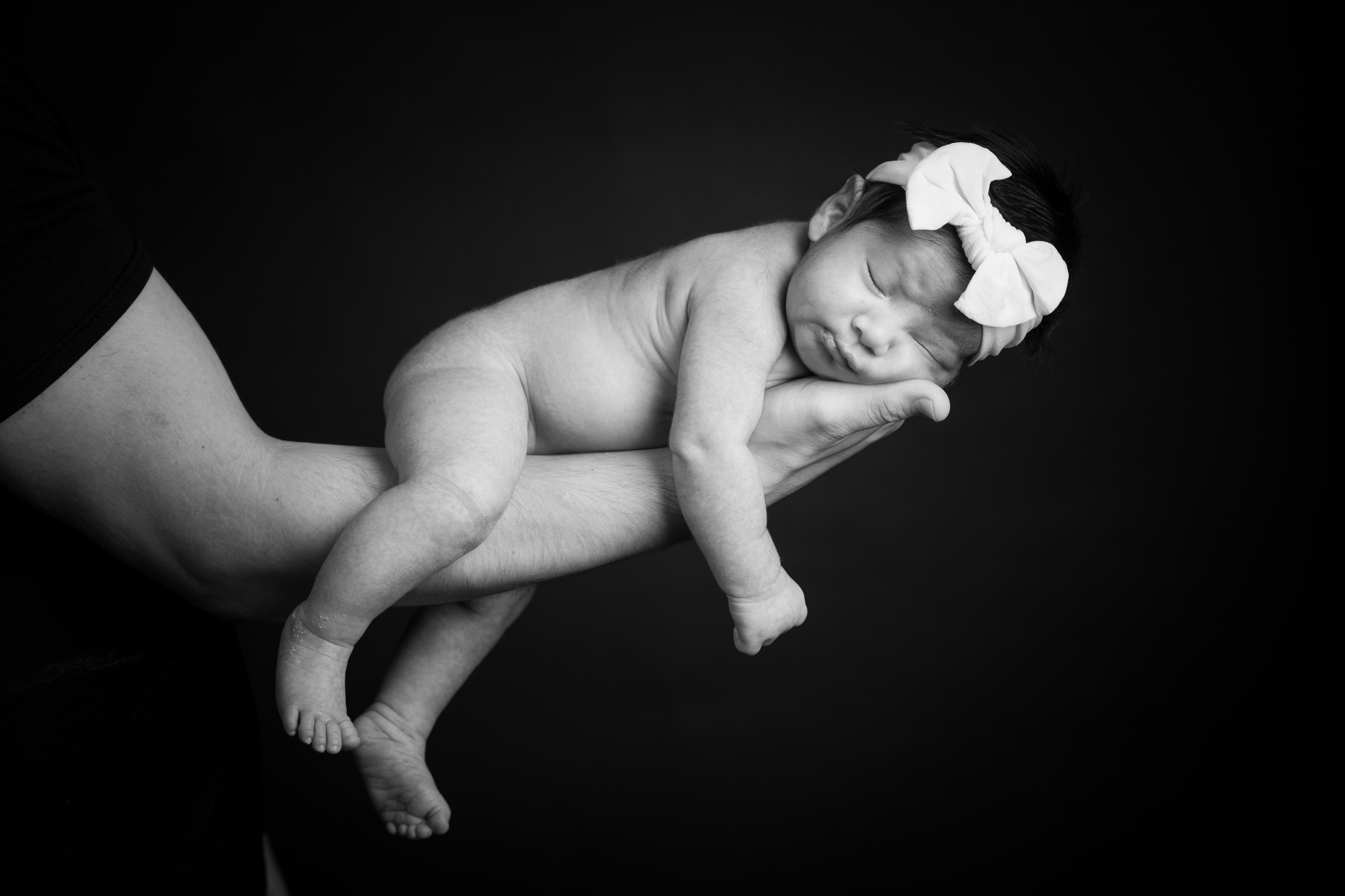 Newborn resting safely across two adult hands in a black-and-white portrait.