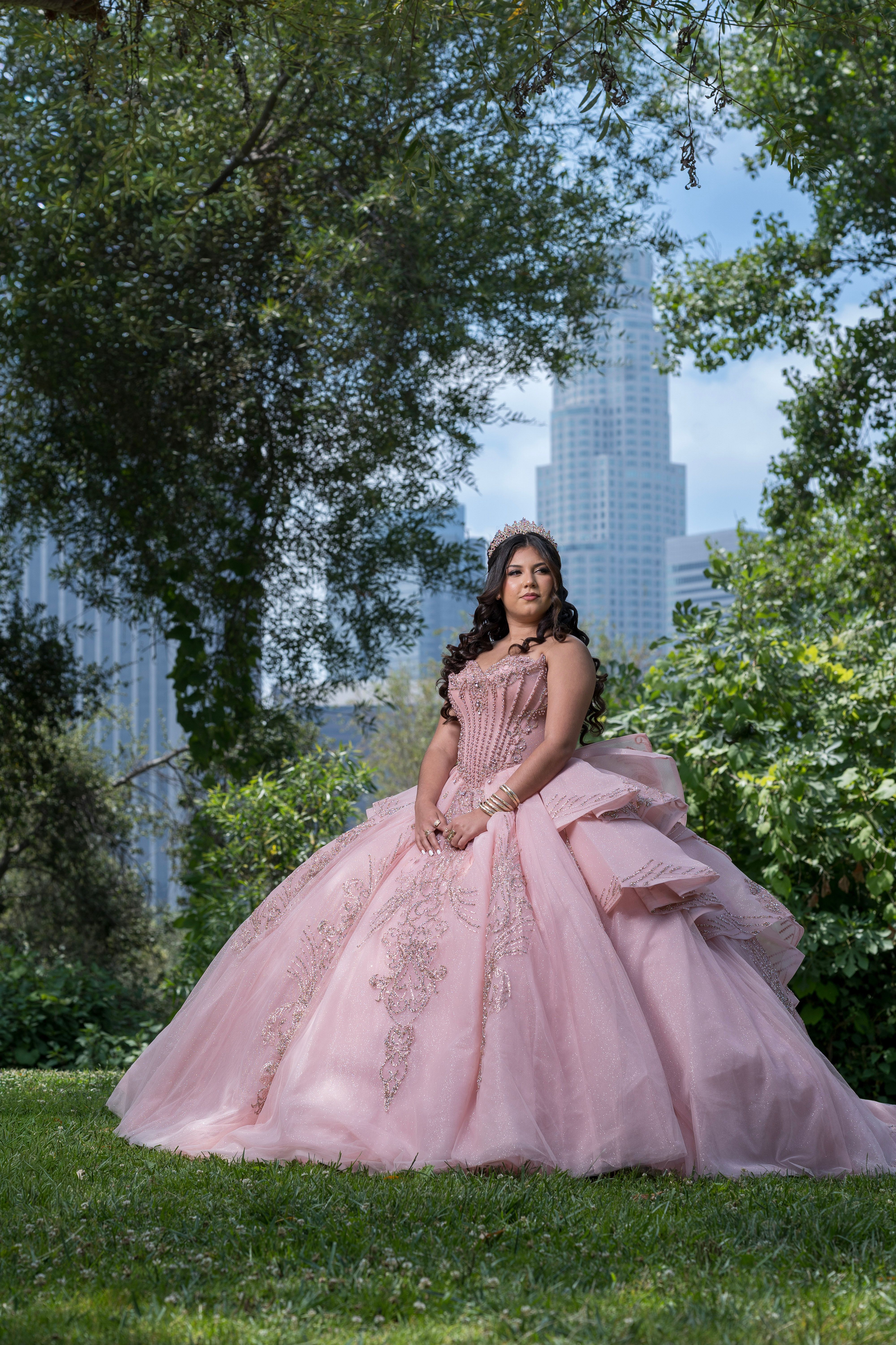 Quinceañera in a pink gown framed by trees and the Los Angeles skyline.